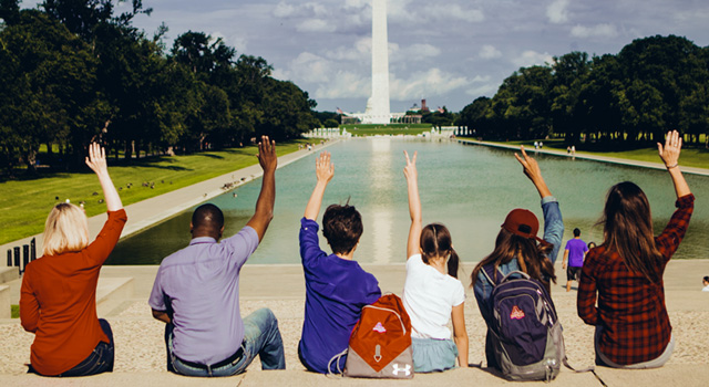 Students with hands raised with the Washington Monument in the background.